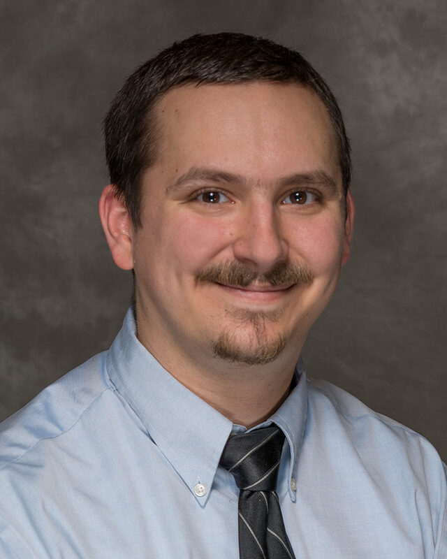 Portrait of Jonathan Enzinna in a light blue shirt and striped tie